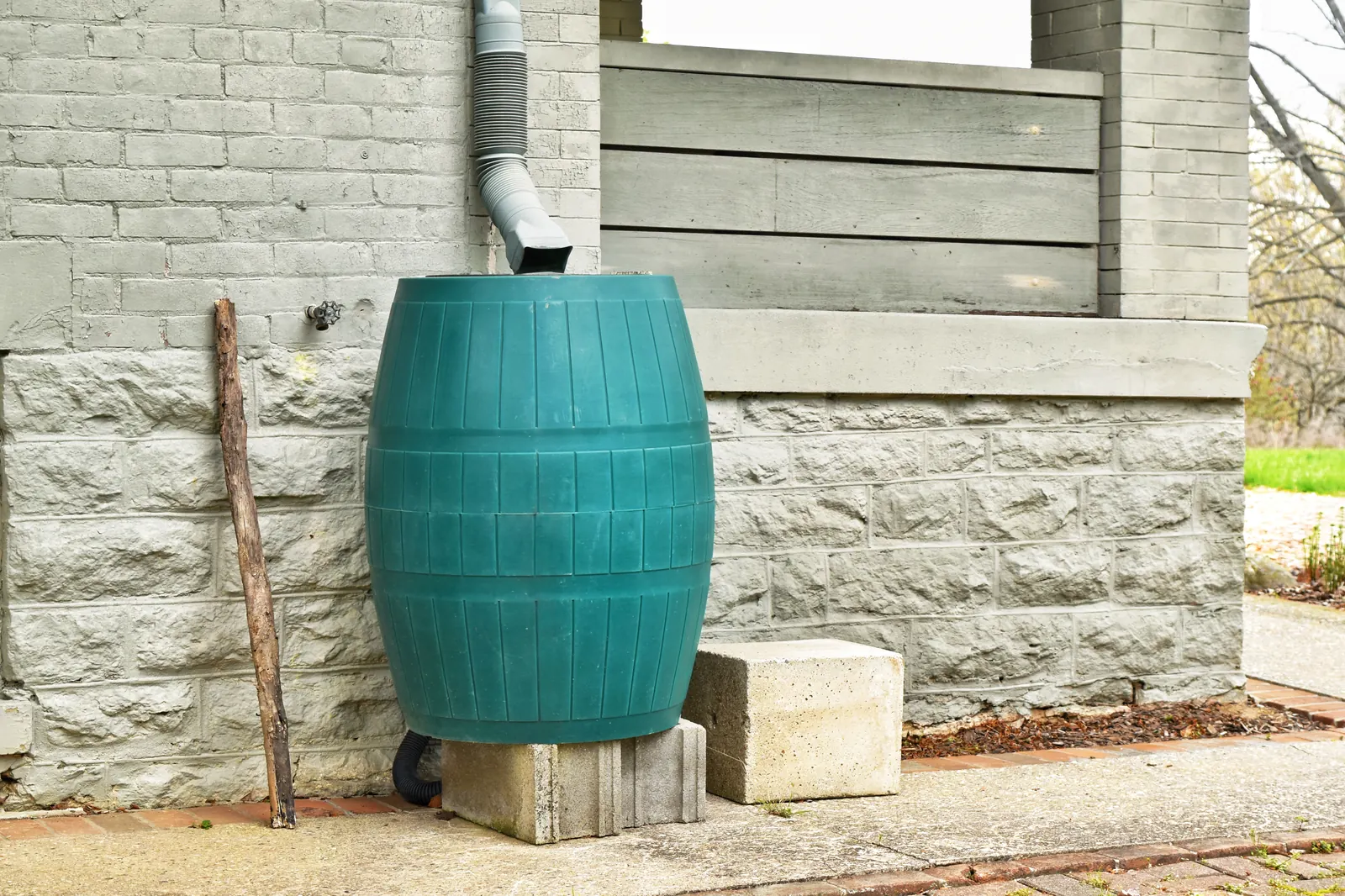 Een groene regenton onder een regenpijp in een tuin